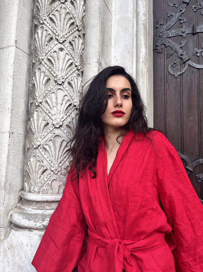 A refined woman adorned in a vibrant cherry red linen kimono stands on the steps of a beautiful old building. Her clothing has been meticulously tailored from top-tier linen, and proudly represents South African design and artistry.