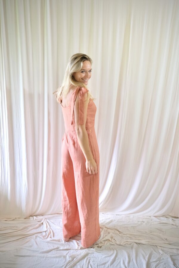 Luxurious pink jumpsuit by bespoke Linen designer on elegant woman smiling and looking back to the camera over her shoulder.