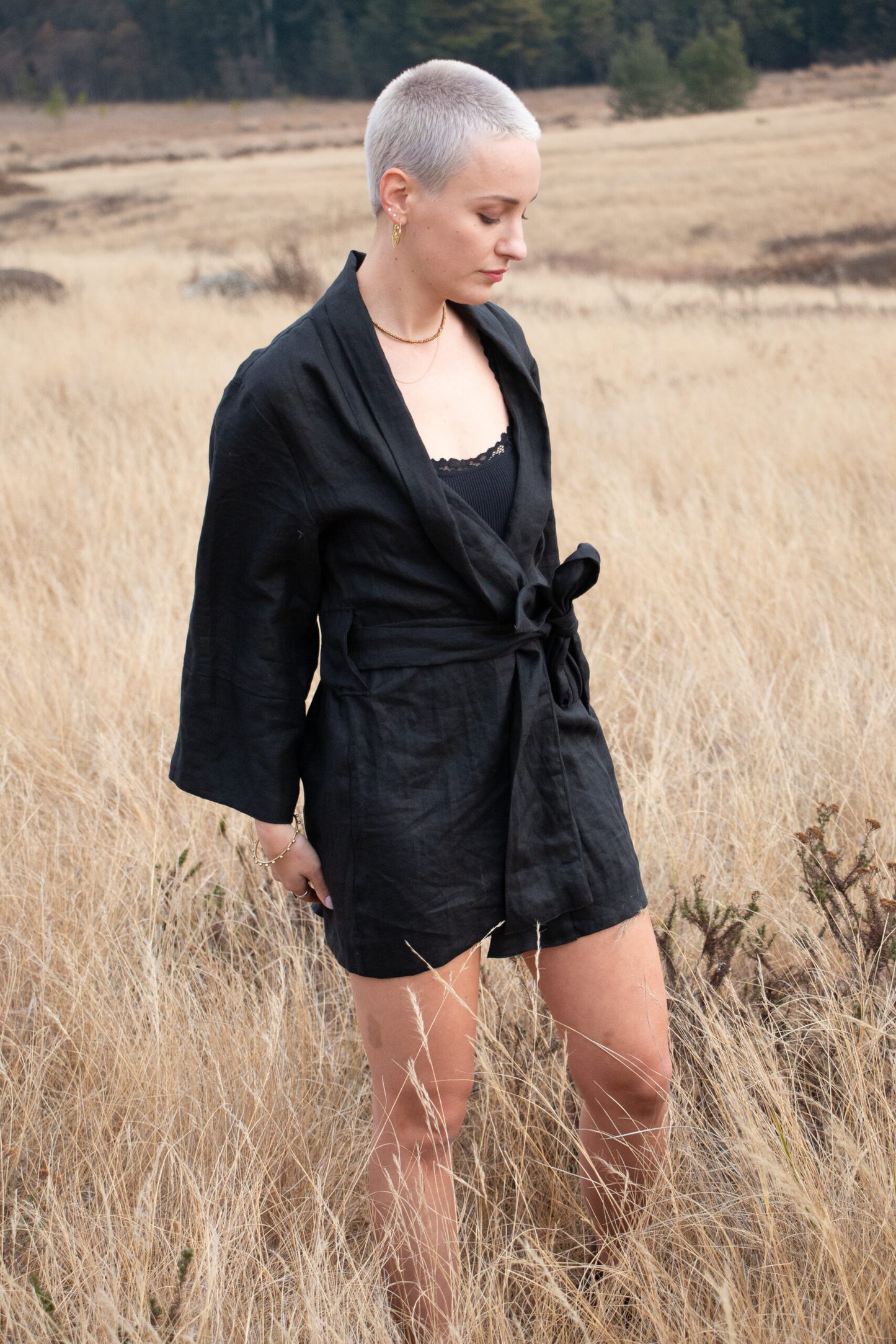 Standing in a field of long brown grass, a stylish and refined women wears a black kimono made of high quality linen fabric. The kimono she wears is designed and manufactured in South Africa.