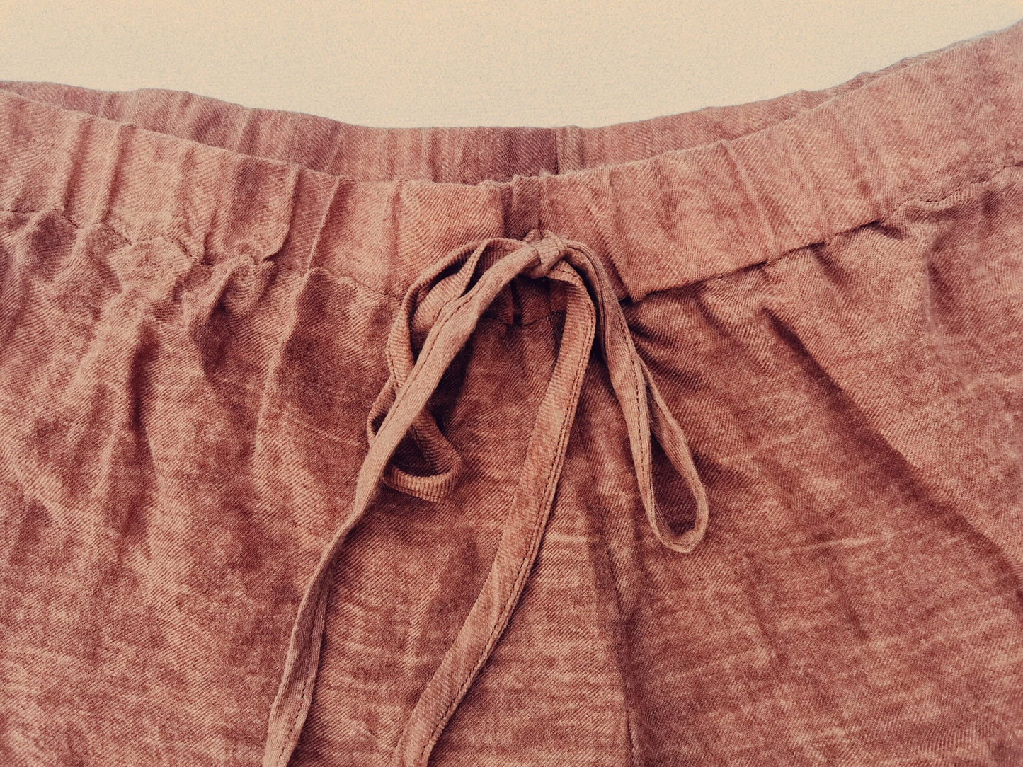A close-up of loungewear shorts made of rust coloured linen fabric. The shorts utilise a draw string for added comfort around the waist. 