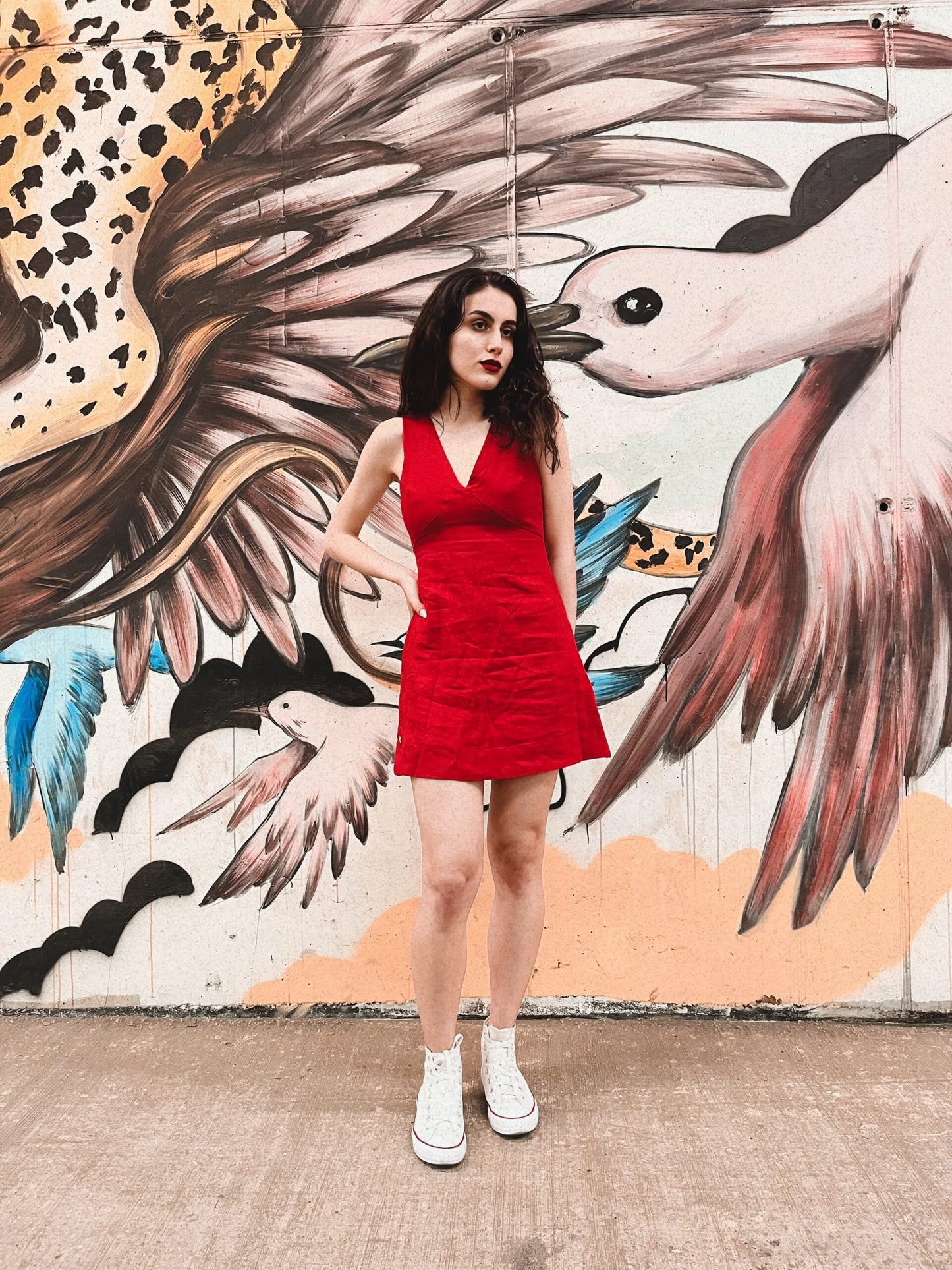 Fashionable woman in exclusive Chery red linen dress stands confidently in front of artistic mural, epitomizing South African elegance in a piece designed and handmade by a South African linen clothing designer.