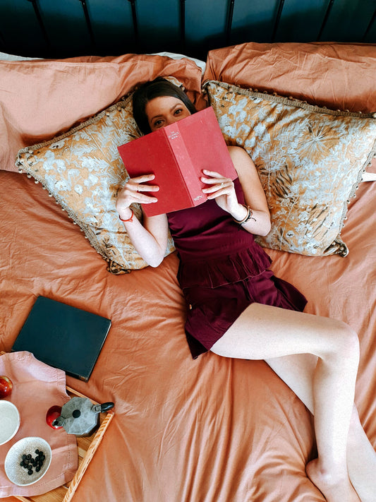 Women lies seductively on a bed whilst reading a book and wearing a linen loungewear set that comprises of a plum coloured linen top and plum coloured linen shorts. Her luxurious loungewear set is designed in South Africa and handcrafted from the finest linen material.