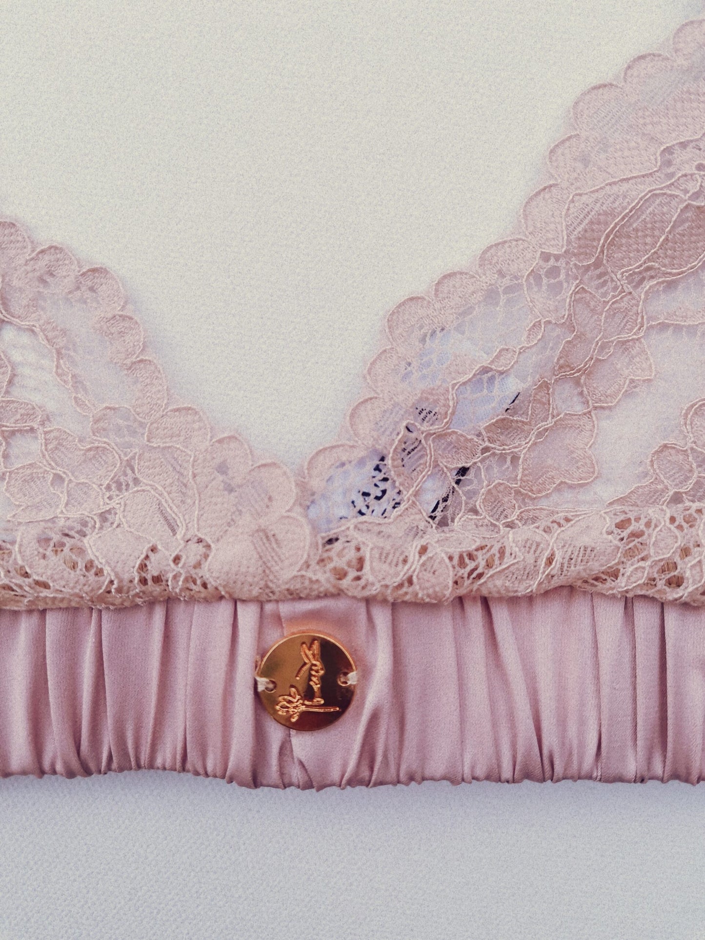 Close up photo of a light pink lace bralet showing the garment details such as the small rose gold logo
